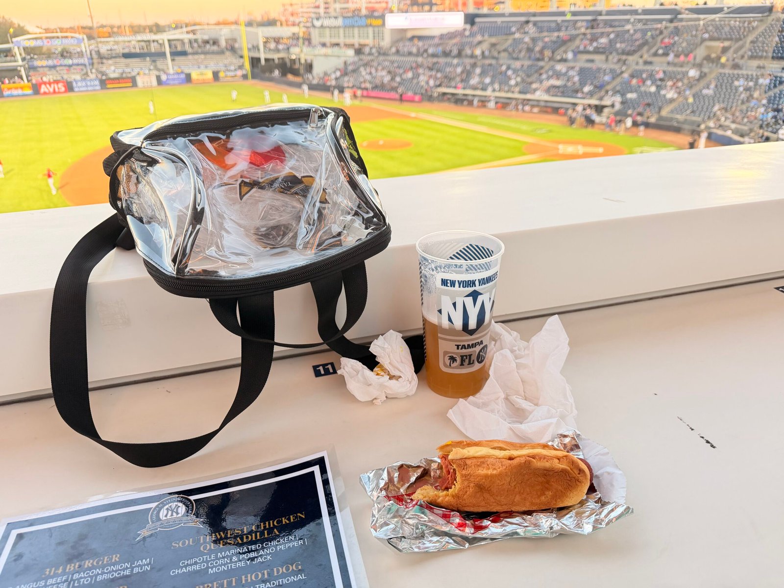 Game-day spread with Sabrett hot dog, beer, menu and clear bag at the seats